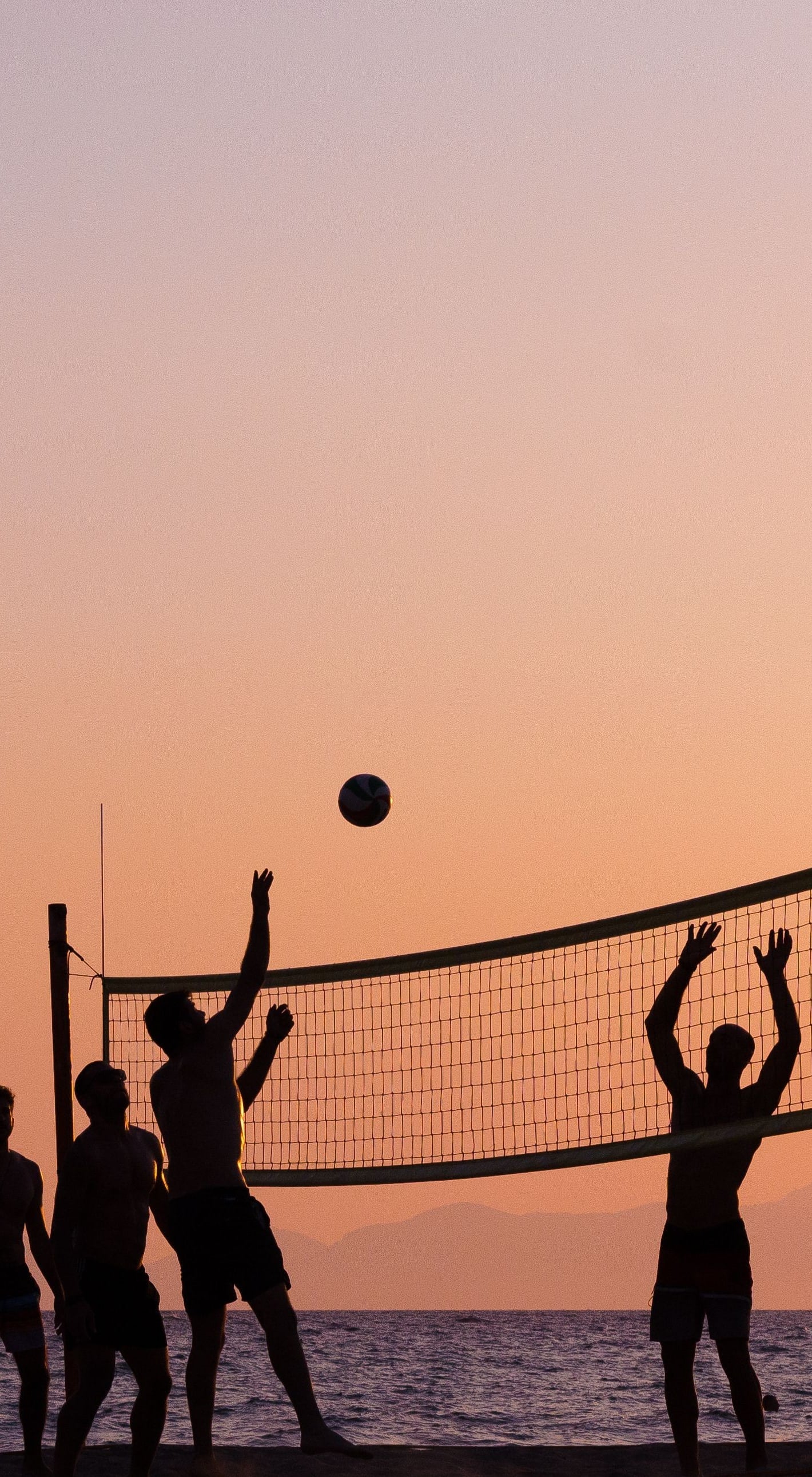 Adults playing beach volleyball at sunset, silhouetted against the sky